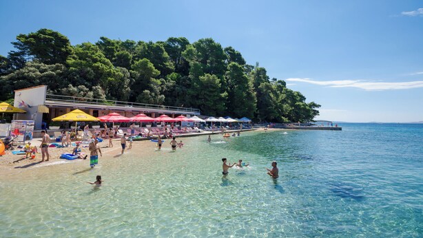 Ein Strand mit klarem Wasser, Sonnenschirmen und Menschen.