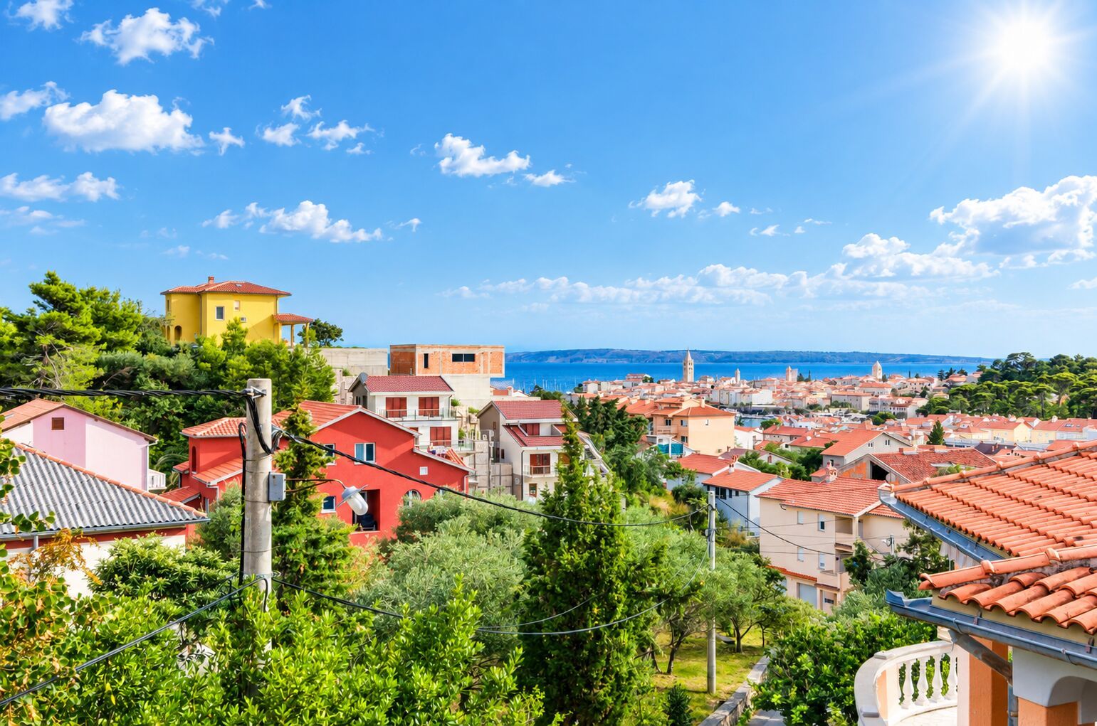 Eine Küstenstadt mit roten Dächern, blauem Himmel und Blick auf das Meer.