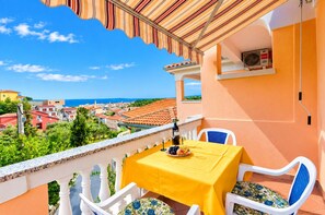 A balcony with a yellow table, white chairs, and a view of the sea and town. - Apartments Darko (Palit)