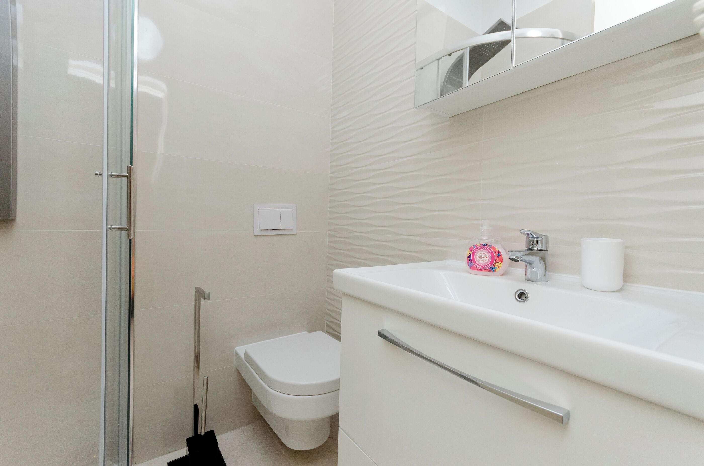 A modern bathroom with a glass shower enclosure, a white toilet, and a sink with a soap dispenser.