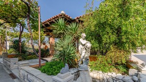 Ein Garten mit einer Statue, Steinmauern und einer Pergola.