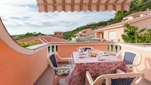 Eine Terrasse mit Tisch und Stühlen für zwei Personen, sowie ein gestreifter Sonnenschirm.
