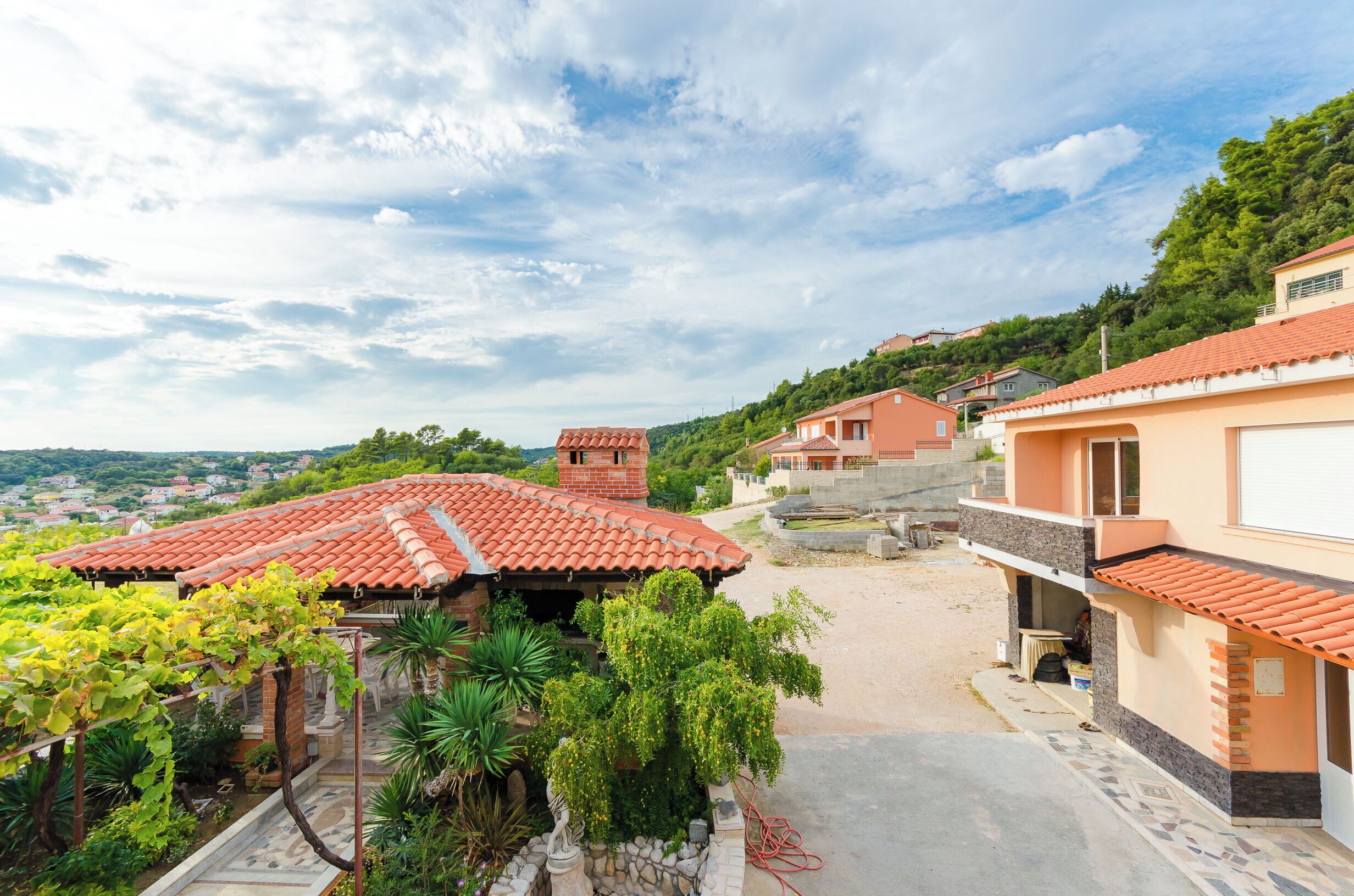 A residential area with terracotta-roofed houses, a paved courtyard, and lush greenery.