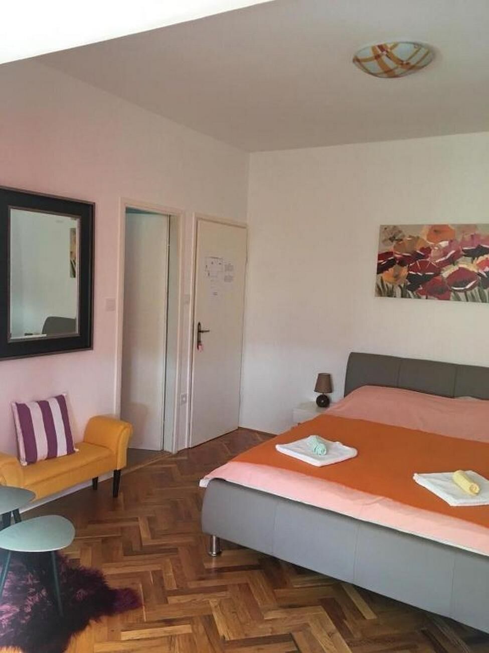 Um quarto com cama, cadeira, escrivaninha e espelho.