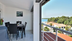 A balcony with a view of the sea and buildings, a dining area with a table and chairs, and a painting on the wall. - Apartments Ester (Funtana)