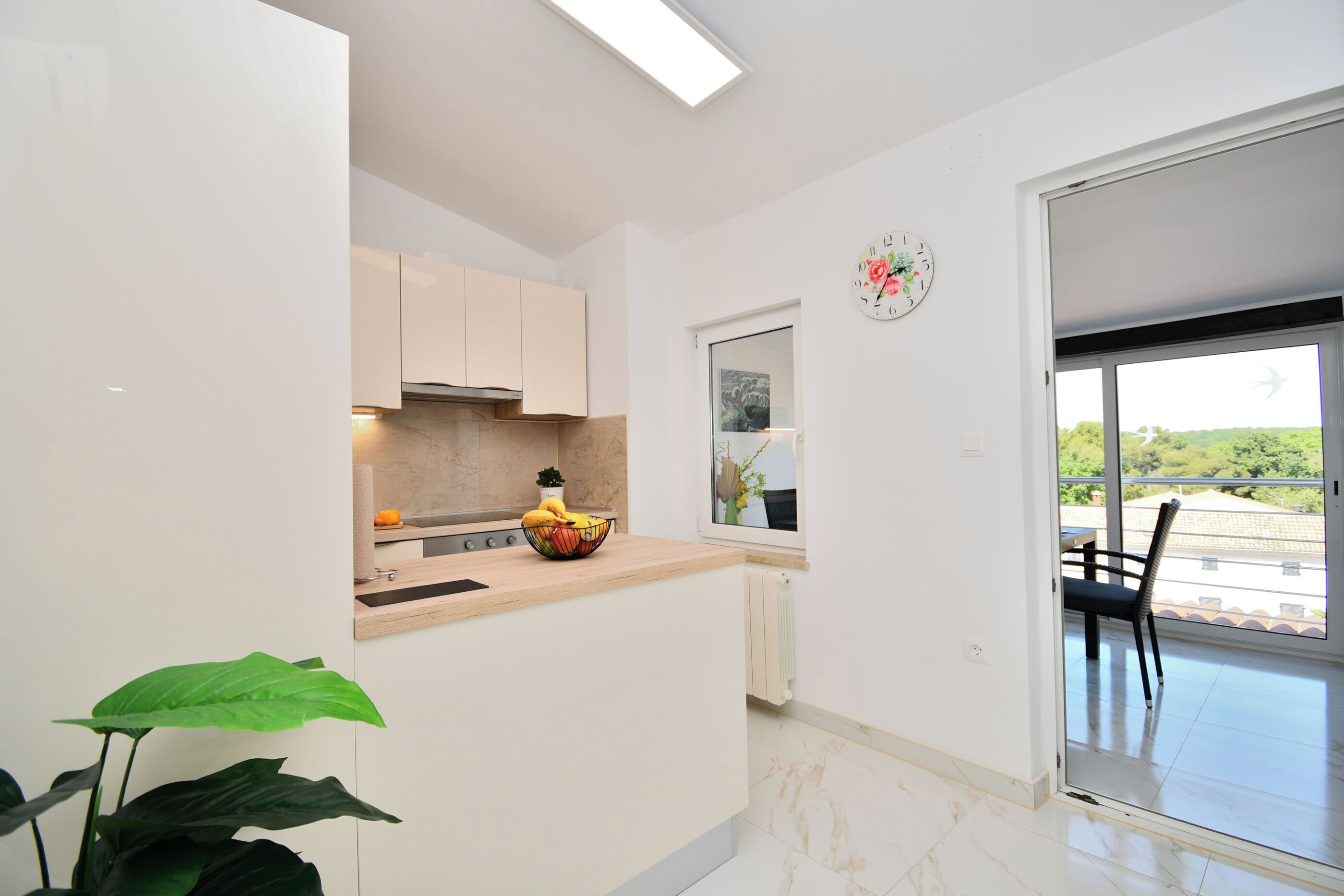 Uma cozinha moderna com uma ilha grande, uma área de refeições com uma cadeira, e vista para o verde através de uma porta deslizante.