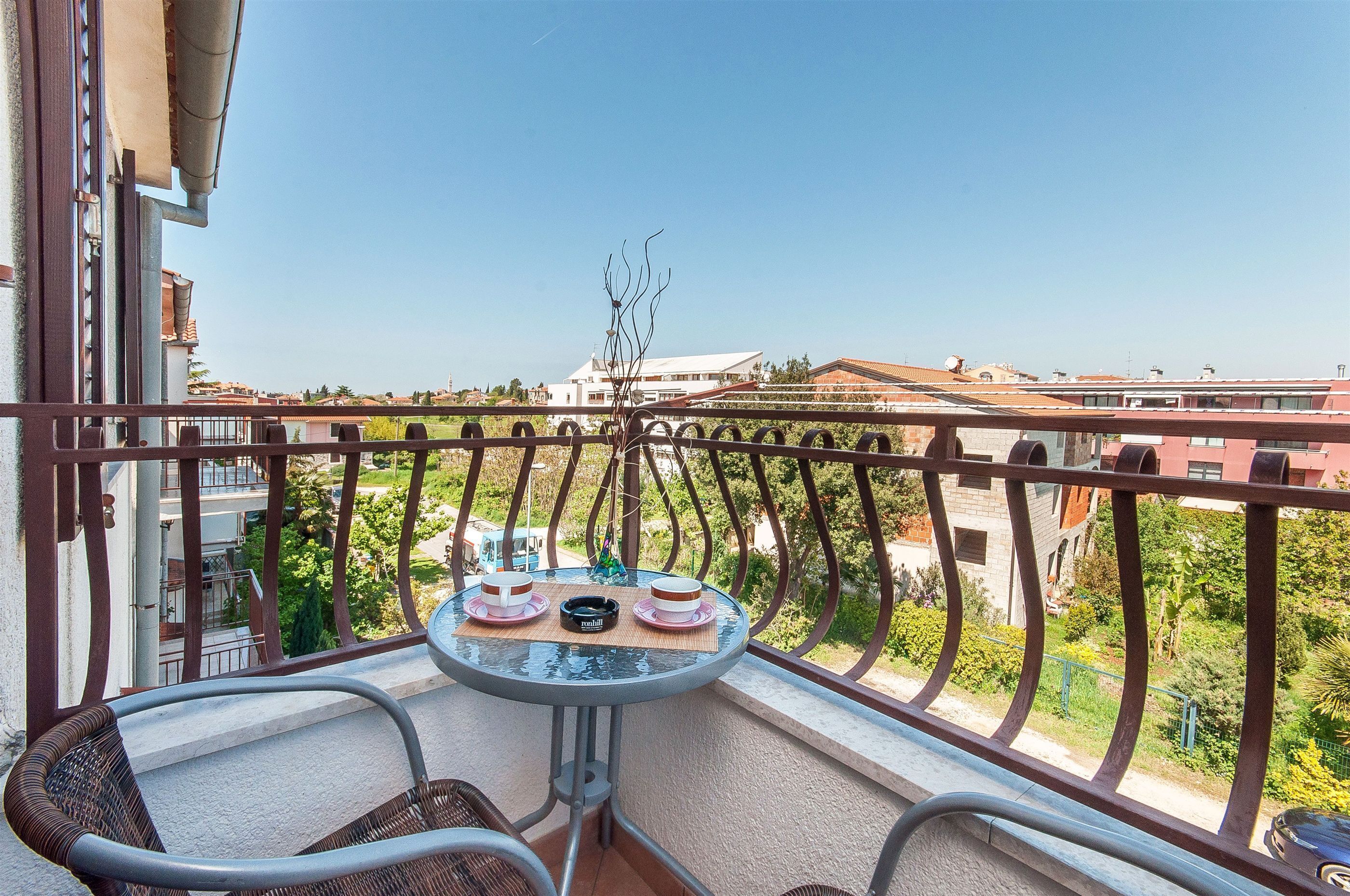 Ein Balkon mit Tisch für zwei Personen, Blick auf eine Wohngegend mit Häusern und Grünflächen.