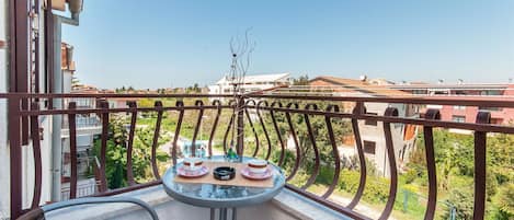 A balcony with a table set for two, overlooking a residential area with houses and greenery.