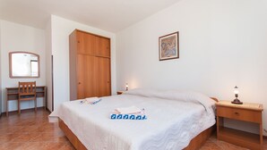 A bedroom with a bed, a wooden wardrobe, a desk with a chair, and a nightstand with a lamp. - Apartments Luciana (Rovinj)