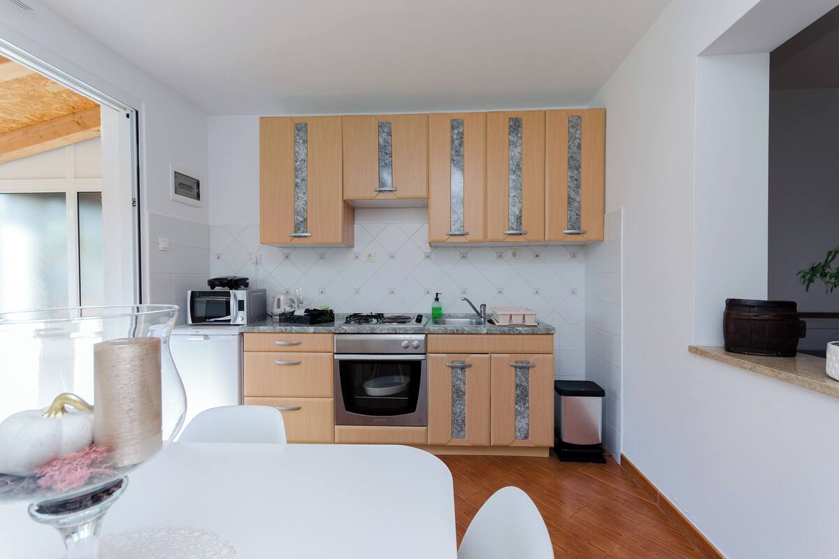 A compact kitchen with wooden cabinets, a microwave, a stove, and a trash bin.