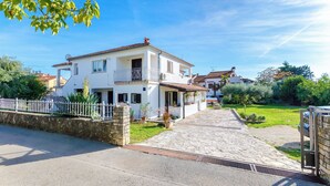 Una casa de dos pisos con entrada de piedra, una cerca blanca y un jardín con diversas plantas.