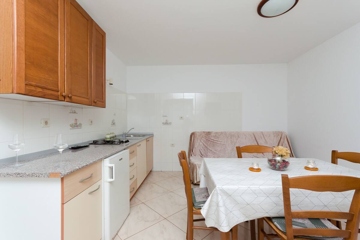 A compact kitchen with wooden cabinets, a granite countertop, and a dining area with a table set for two.