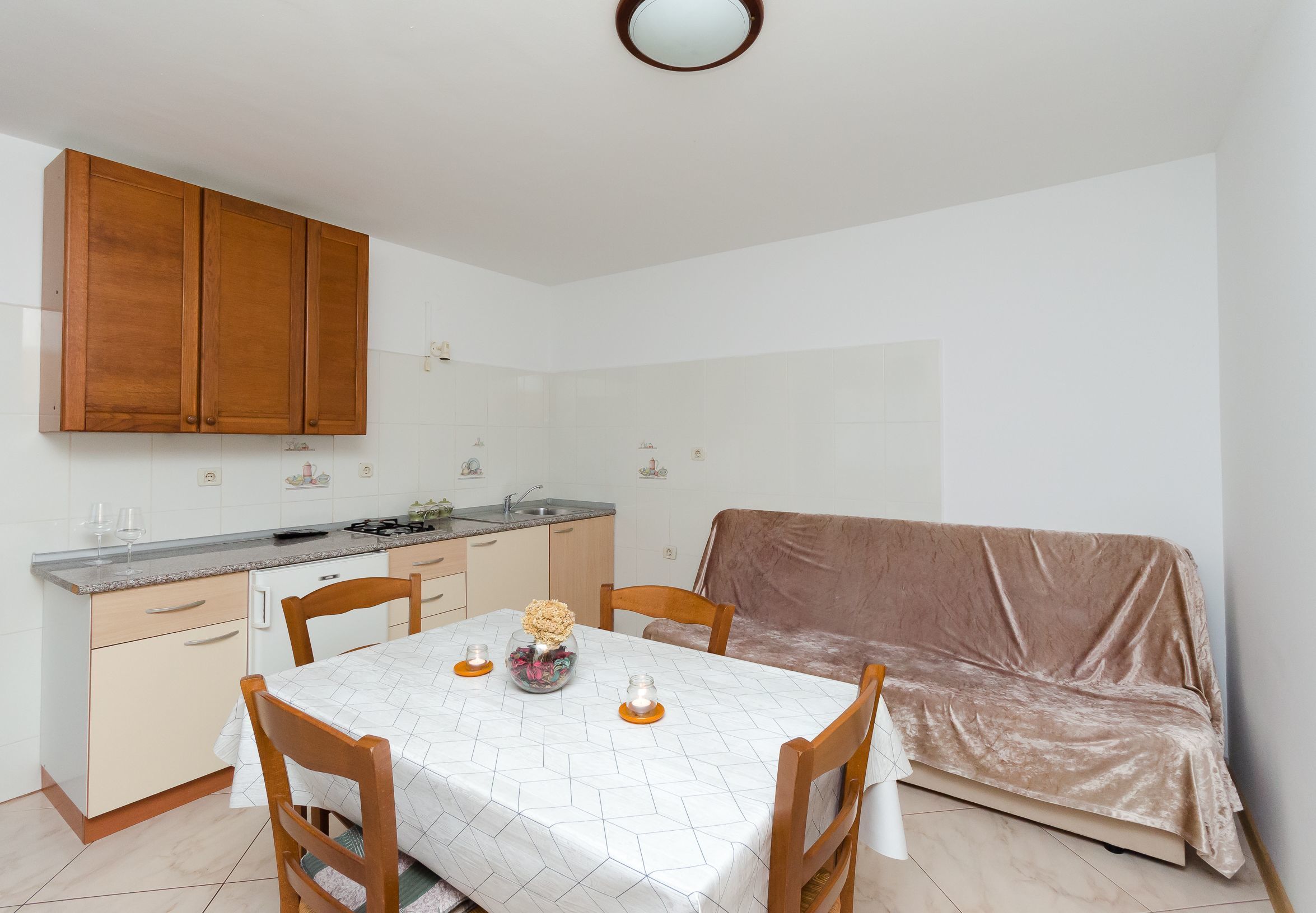 Eine kompakte Küche mit Holzausstattung, einem Esstisch mit Stühlen und einem abgedeckten Sofa.