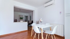 Un comedor moderno con una mesa y sillas blancas, una planta en maceta y un equipo de aire acondicionado en la pared.