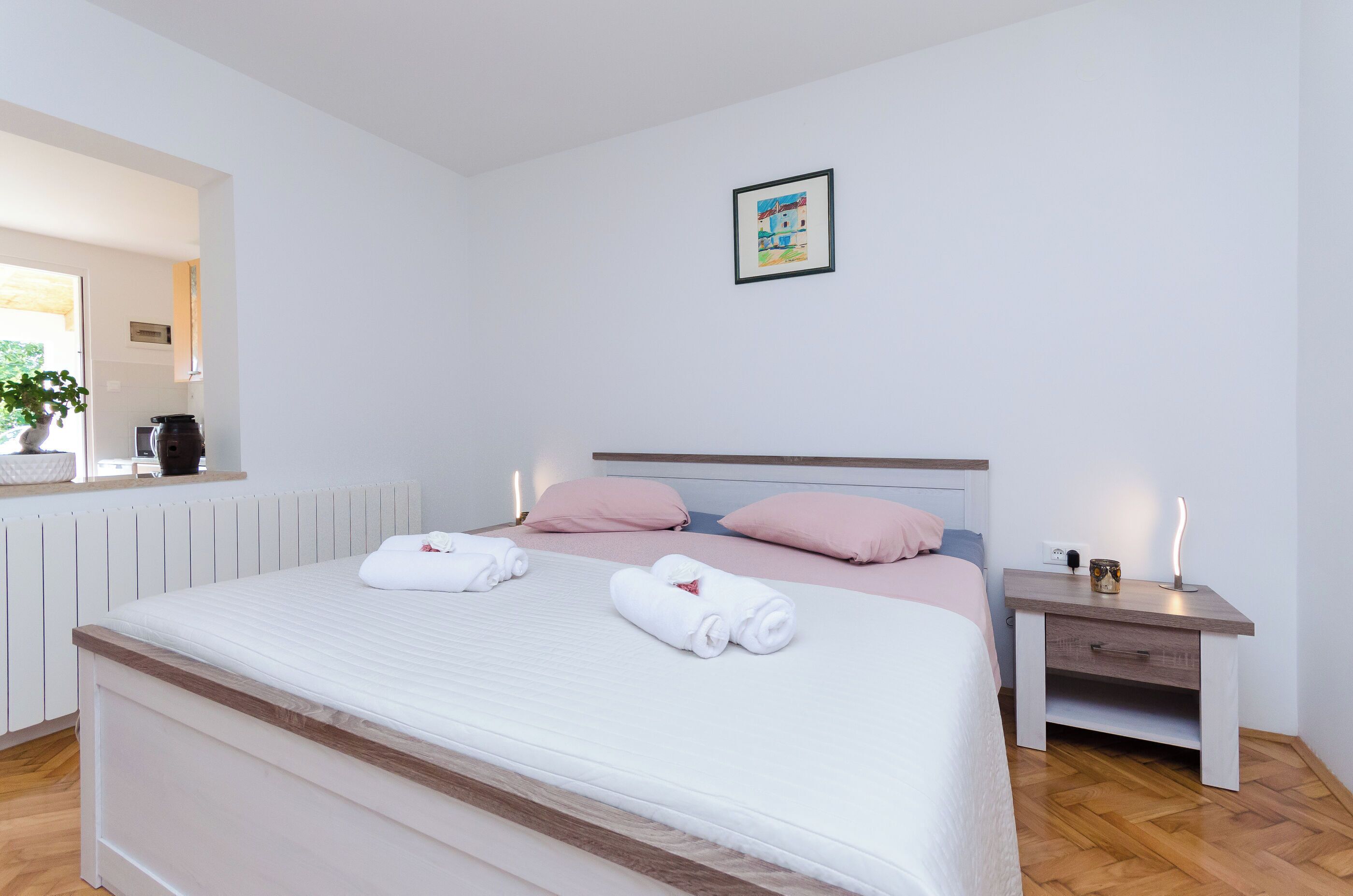 Een netjes opgemaakt bed met twee opgerolde handdoeken, een nachtkastje met een lamp en een lijst met een afbeelding aan de muur.