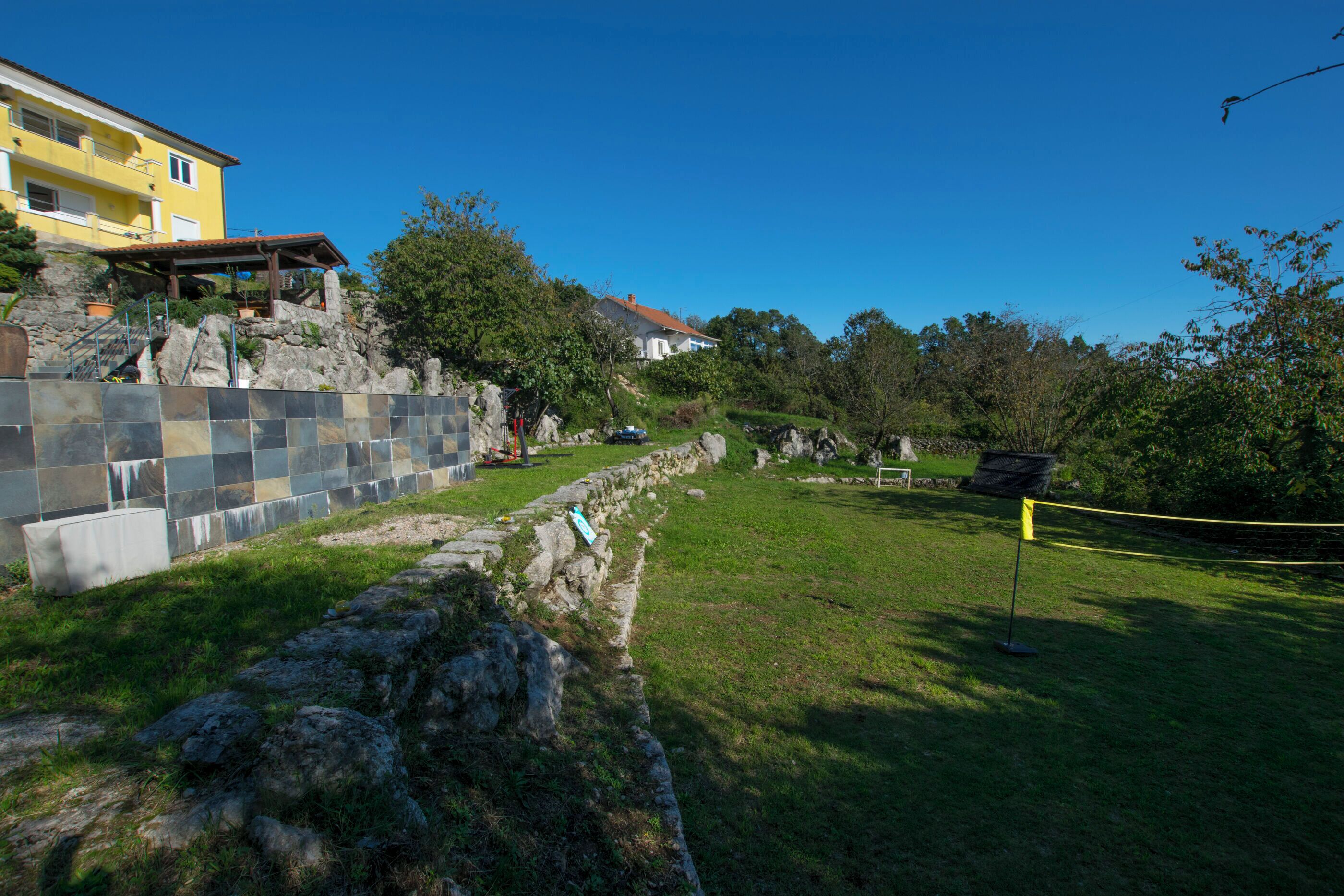 A stone retaining wall with a grassy area and a yellow building in the background.