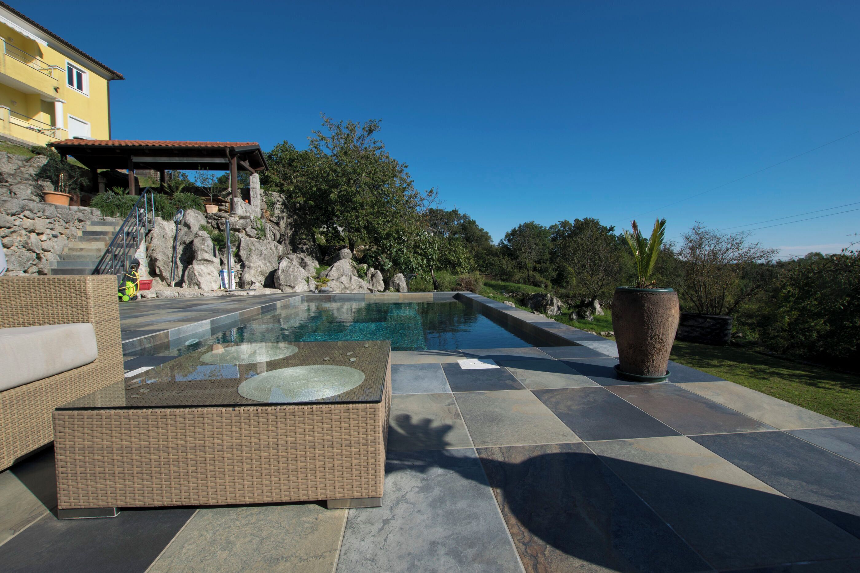 A swimming pool with a glass top, surrounded by stone steps and a wicker sofa.