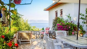 A patio with stone flooring, white plastic chairs, a table, and potted plants. - Apartment Andreas (Ravni)