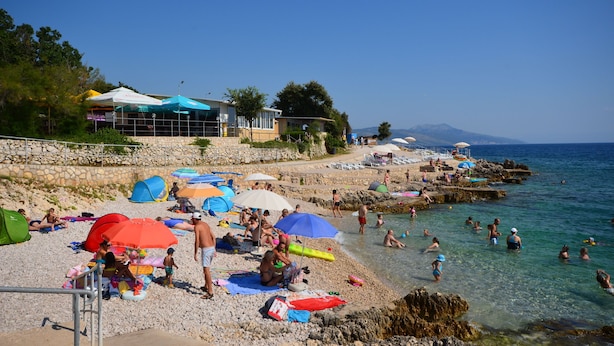 A beach with umbrellas, people, and a building with a blue roof. - Apartment Andreas (Ravni)