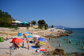 Een strand met parasols, mensen en een gebouw met een blauw dak.