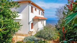 A white building with a red-tiled roof, wooden shutters, and a view of the sea. - Apartment Andreas (Ravni)