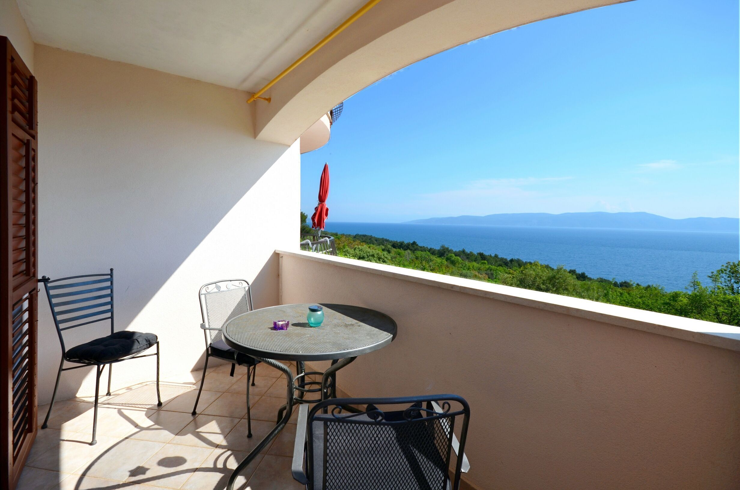 A balcony with a table and chairs, overlooking a scenic view of the sea and greenery.