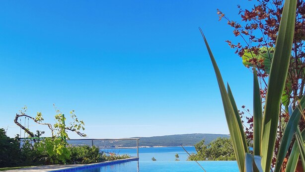 Ein klares, blaues Schwimmbecken mit Blick auf das Meer und die dahinterliegenden Hügel.