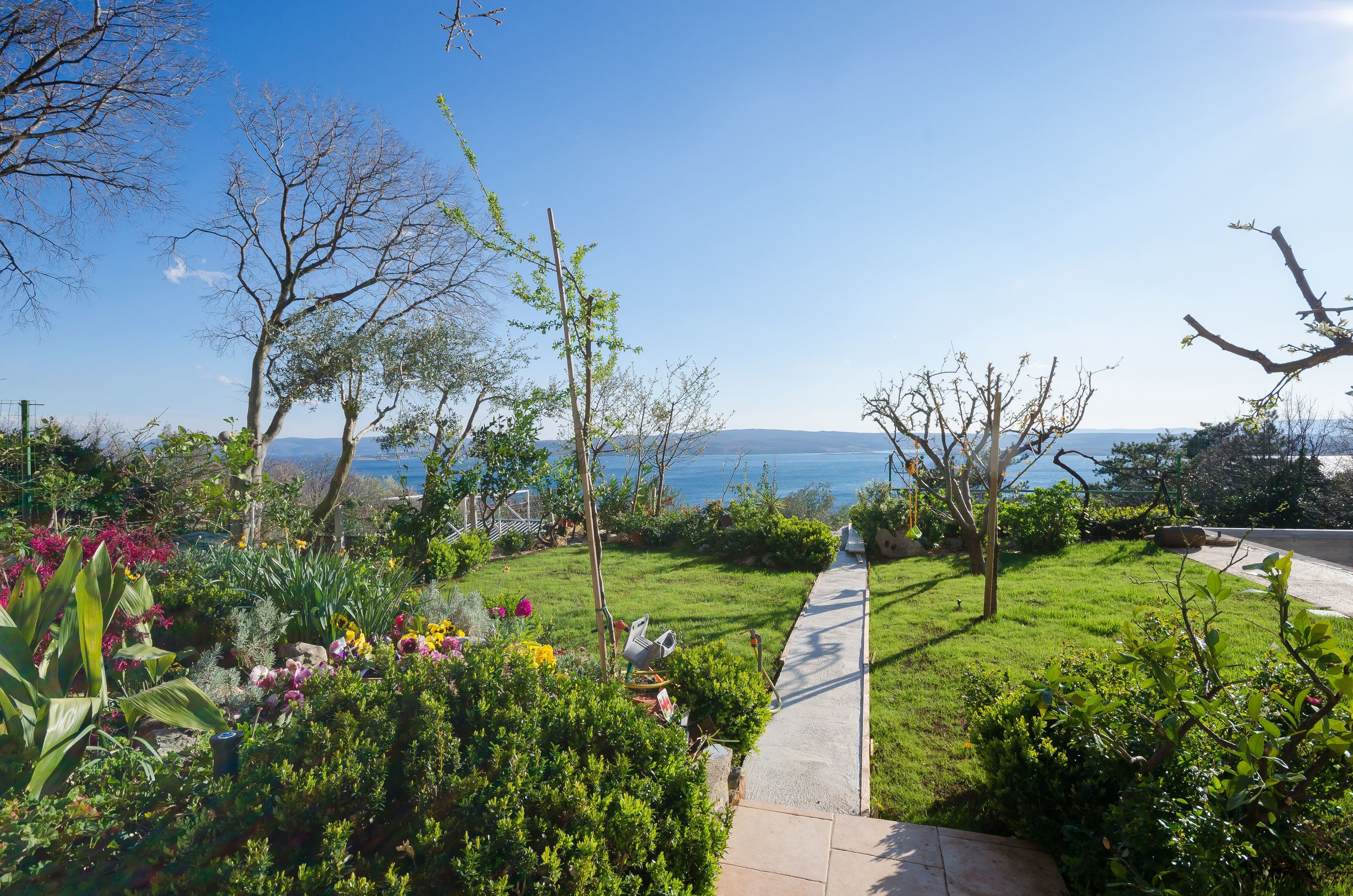 A garden with a pathway leading to a scenic view of the sea.