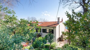 Ein Haus mit rotem Ziegeldach, umgeben von üppiger Vegetation und blühenden Pflanzen.