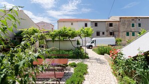 A courtyard with a paved path, a bench, and a table. - Apartments Puntica (Punat)