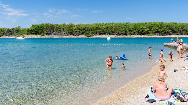 A beach with clear water, people swimming, and a boat in the distance. - Apartments Puntica (Punat)