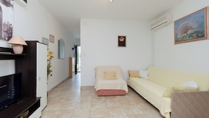 A living room with a sofa, a television, and a small table with a lamp. - Apartments Puntica (Punat)