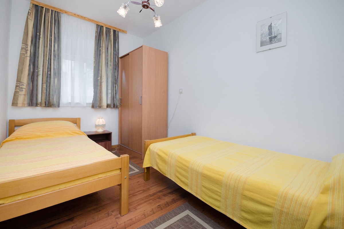 A bedroom with two beds, a wardrobe, a bedside table with a lamp, and a framed picture on the wall.