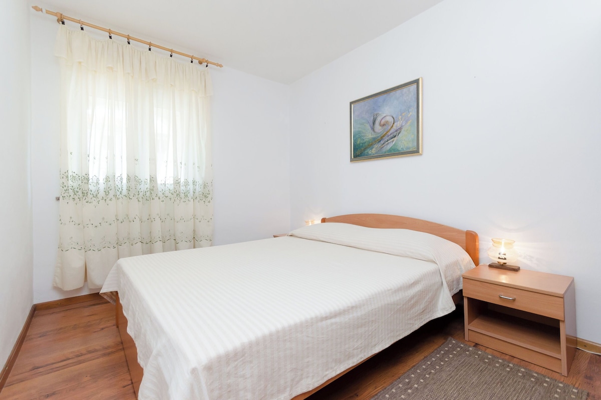 A neatly made bed with a wooden headboard, a bedside table with a lamp, and a painting on the wall.