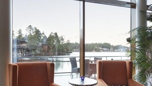 Two armchairs with zebra-patterned cushions, a round table, and a large window offering a view of a lake and buildings. - Dyreparken Safarihotell (Kristiansand)