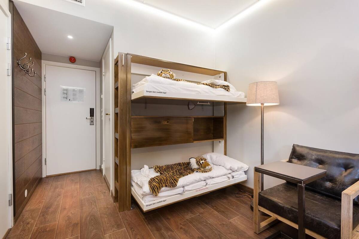 Uma cama de beliche com um brinquedo de tigre macio na cama inferior, uma mesinha de cabeceira, um abajur e um sofá.