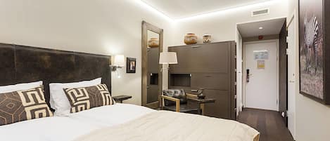 Habitación de hotel con una cama grande, un escritorio, una silla, un espejo y una puerta que da a otra habitación.
