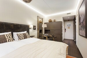 Habitación de hotel con una cama grande, un escritorio, una silla, un espejo y una puerta que da a otra habitación.