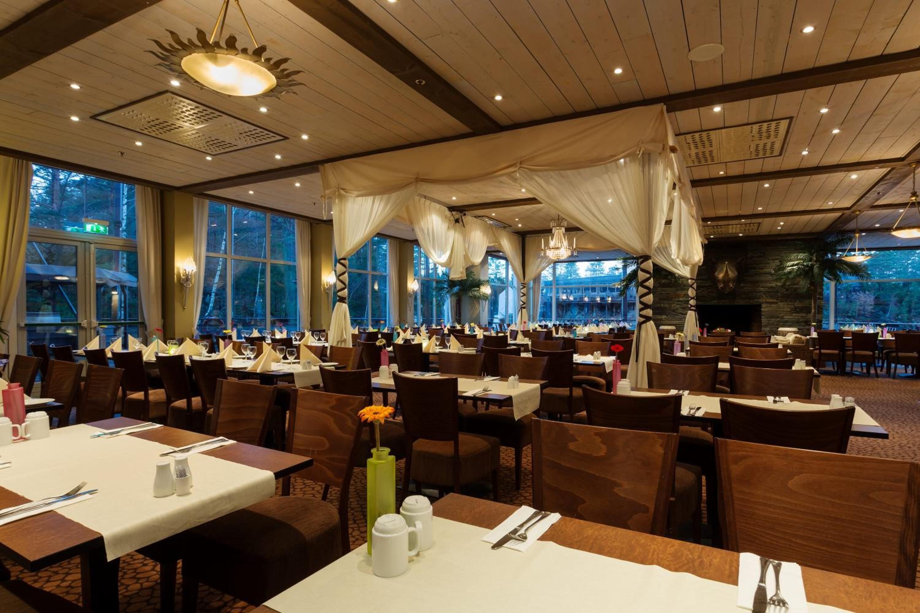 A spacious dining area with multiple tables and chairs, large windows, and a chandelier.