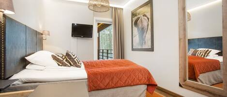 A hotel room with a bed, a desk, a chair, a television, a large mirror, and a framed picture on the wall.