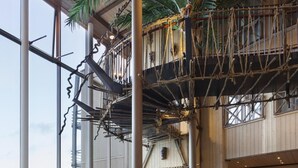 A spacious indoor area with a high ceiling, large windows, and a view of the outdoors. There are multiple seating areas with sofas and chairs, and a staircase with a rope bridge. - Dyreparken Safarihotell (Kristiansand)