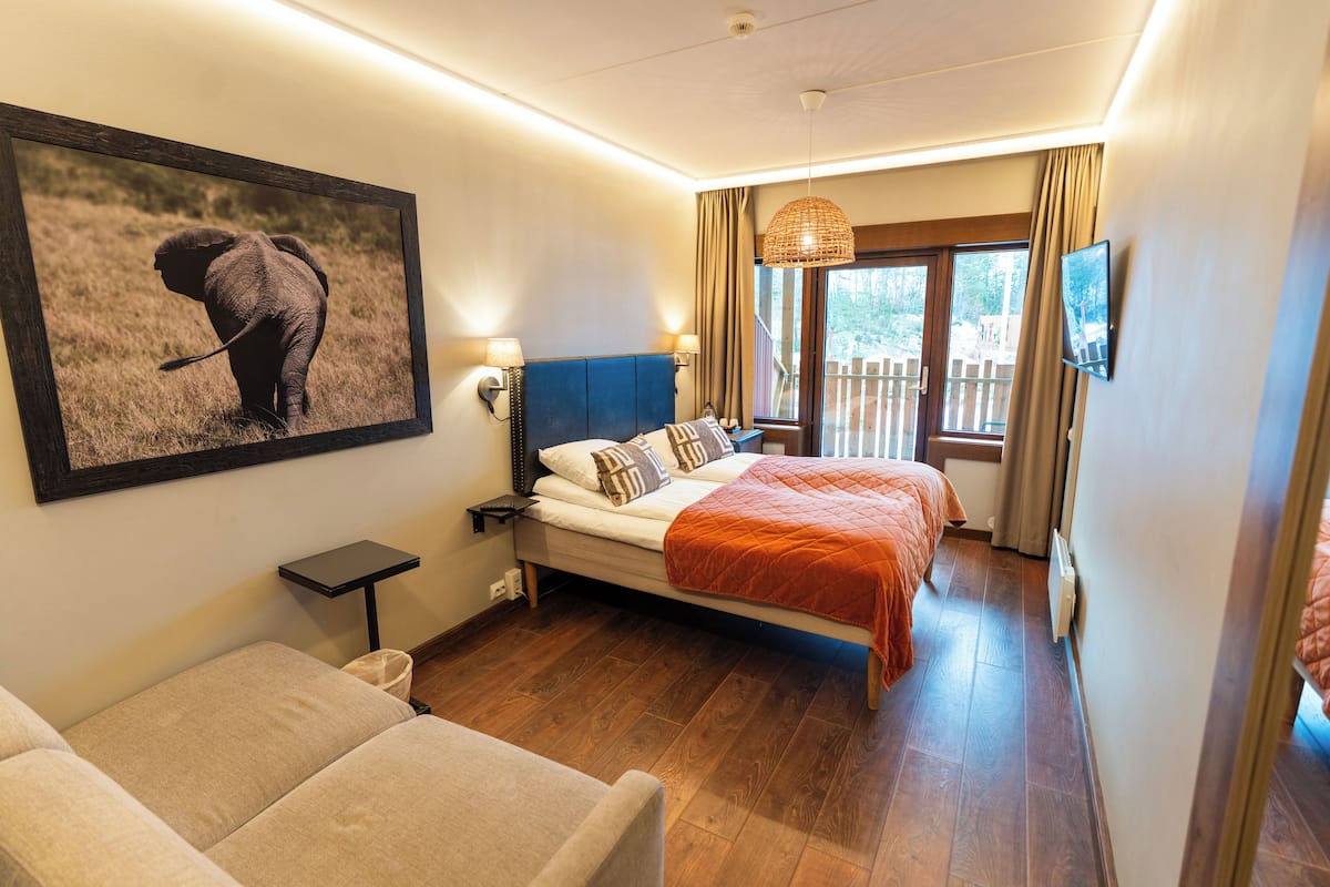 Quarto com cama, mesa de cabeceira, abajur, moldura e vista para o exterior.