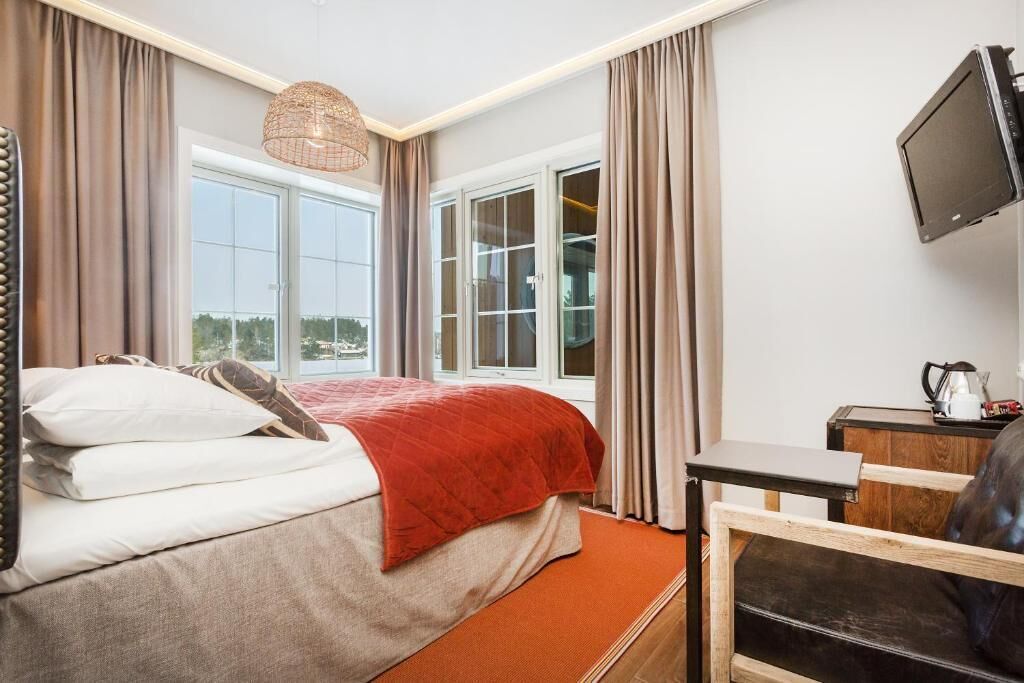Ett hotellrum med en säng, ett skrivbord, en stol, en tv och ett fönster med gardiner.