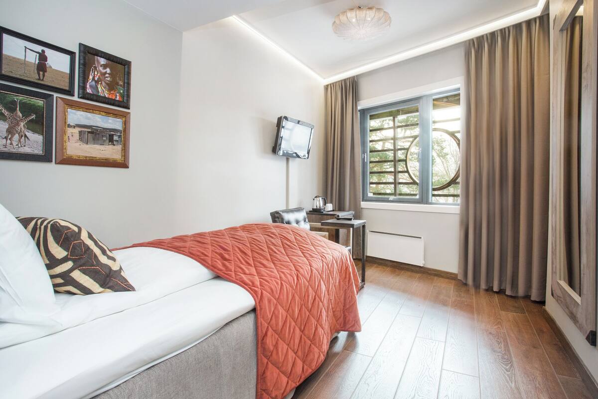Quarto de hotel com cama, escrivaninha, televisão e janela com cortinas.