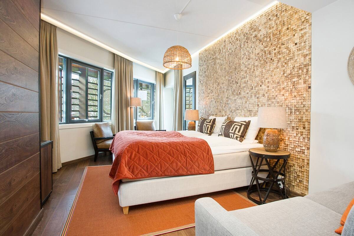 Quarto de hotel com uma cama grande, um sofá, uma mesinha, um abajur e uma parede com textura.