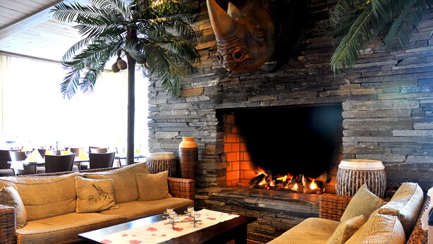 A cozy lounge area with a stone fireplace, wicker furniture, and a large plant. - Dyreparken Safarihotell (Kristiansand)