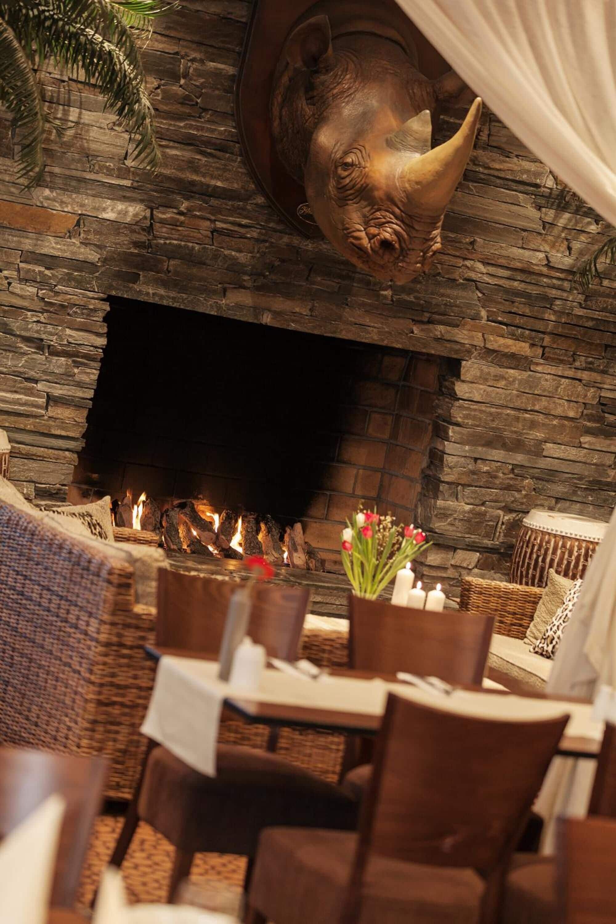 A restaurant with a stone fireplace, wicker furniture, and a decorative animal head above the fire.