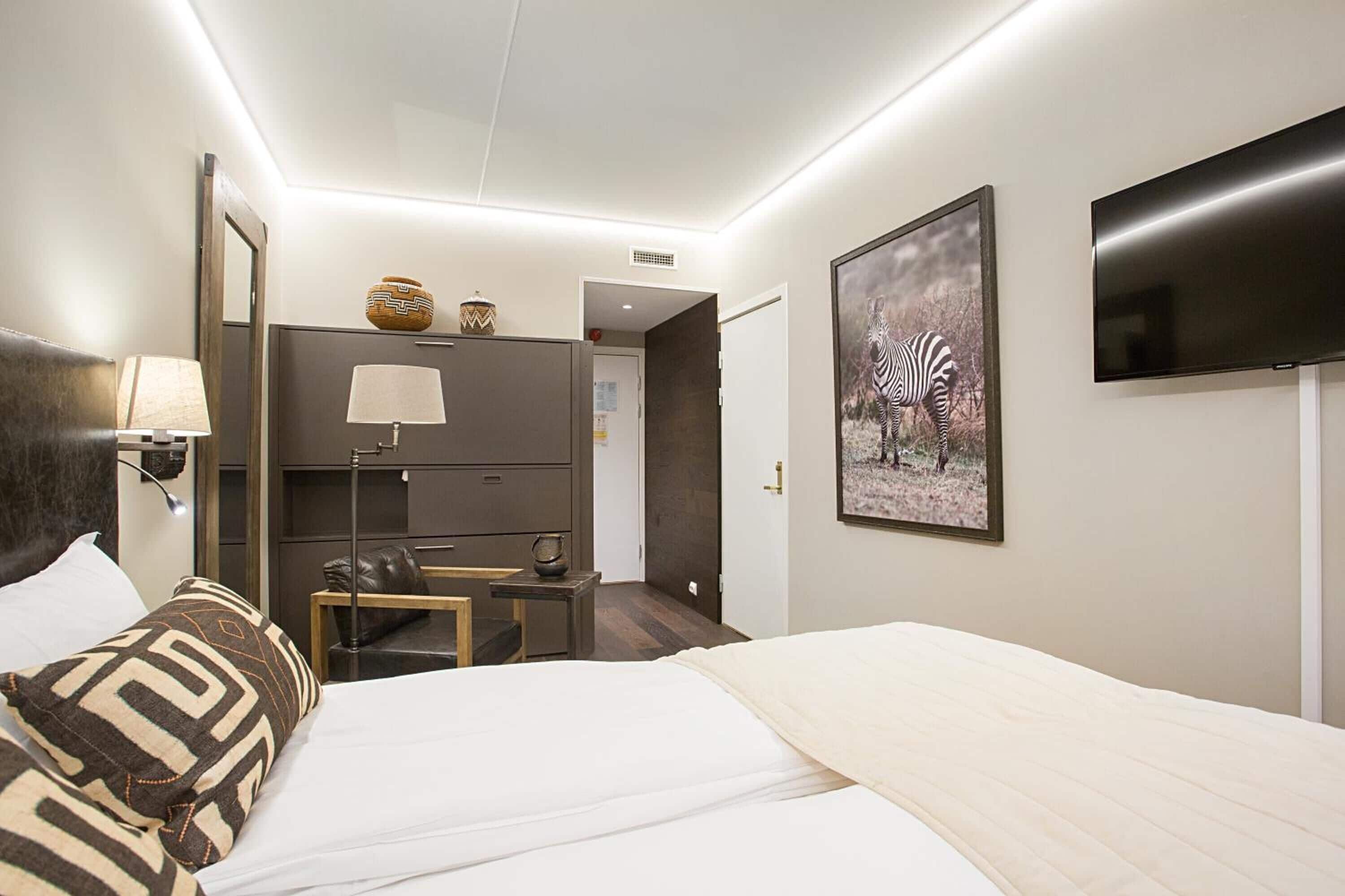 Een hotelkamer met een bed, een bureau, een stoel, een lamp, een televisie en een ingelijst beeld aan de muur.