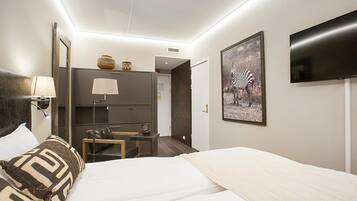 Een hotelkamer met een bed, een bureau, een stoel, een lamp, een televisie en een ingelijst beeld aan de muur.