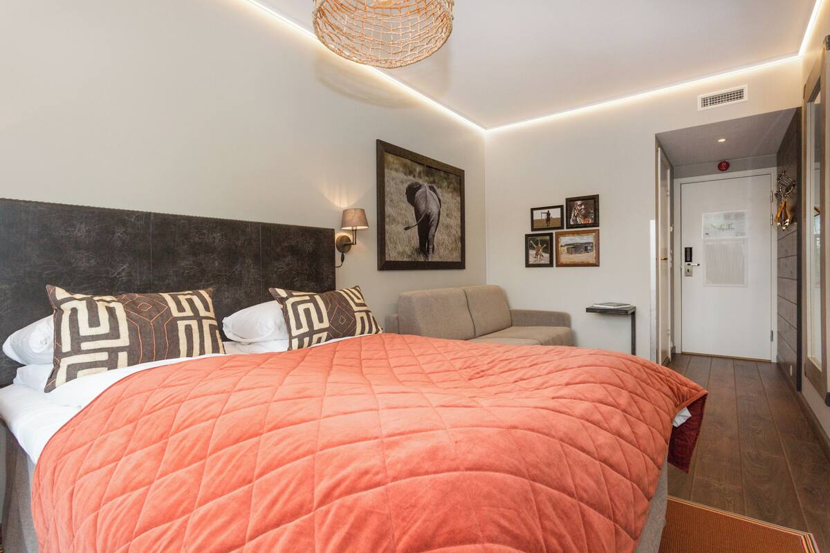 Quarto de hotel com uma cama grande, cabeceira, luminária fixada na parede e um quadro emoldurado.